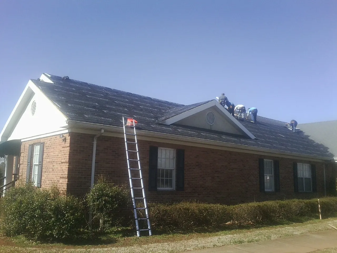 Crew tearing shingles off a brick ranch roof with a ladder set — Metal Roof Repair work by our crew in Eau Claire