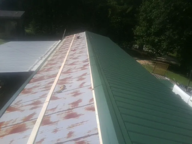 Old rusted panels beside newly installed green metal roofing — Wind Damage Roof Repair by Roofing Brothers in Eau Claire