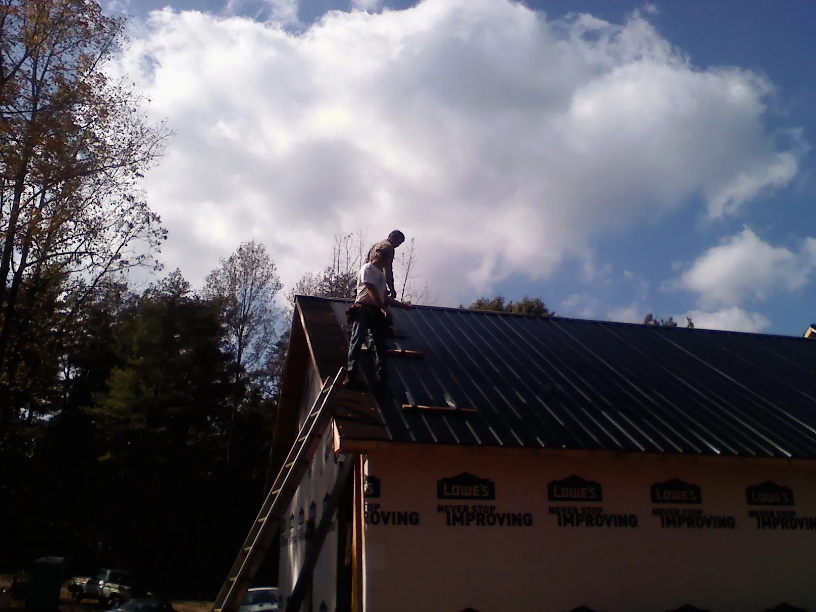 Roofer fastening dark metal panels high against a cloudy sky, from a Roof Inspection job in Eau Claire
