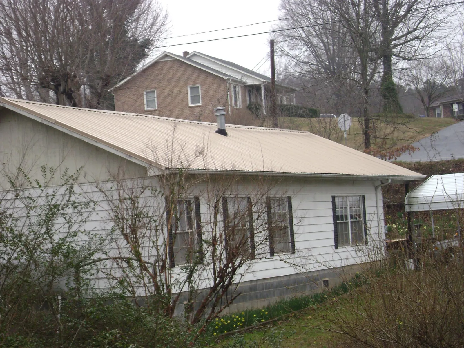 Tan metal roof on a white sided house set into a hillside — Commercial Roofing by Roofing Brothers in Eau Claire